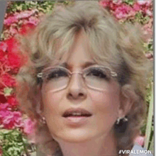 a woman wearing glasses and earrings is standing in front of a bunch of flowers .