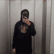 a man taking a picture of himself in an elevator wearing a black hoodie that says ' uae '