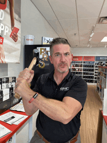 a man wearing a black gnc shirt is holding a wooden stick