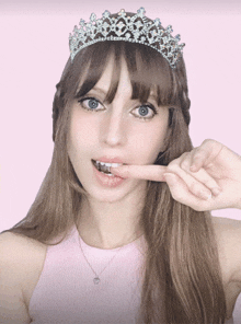 a woman wearing a tiara and a pink tank top bites her finger