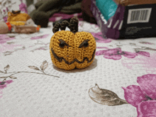 a crocheted pumpkin sits on a bed with purple and white flowers