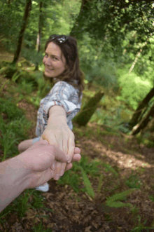 a woman holding a man 's hand in a forest