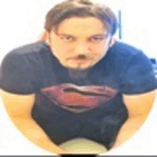 a man wearing a superman shirt is sitting in a circle with his hands folded .