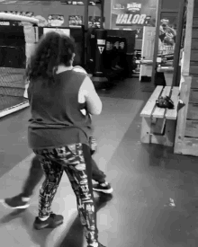 a black and white photo of a woman boxing in a gym with a sign on the wall that says valor