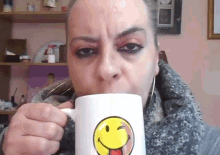 a woman is drinking from a mug that has a smiley face on it