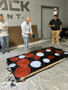 a man pours red white and blue paint on a black surface in front of a sign that says ack nt tm