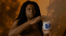 a shirtless man with dreadlocks is holding a jar of petroleum jelly .