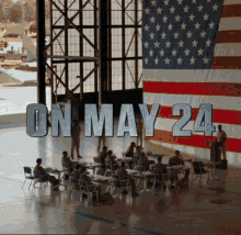 a group of people sit at tables in front of a large american flag with the words " on may 24 " above them