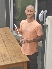 a man in an orange shirt holds a spoon and a mug