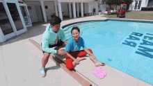 a man and a woman sit on the edge of a swimming pool with a sign that says team rar