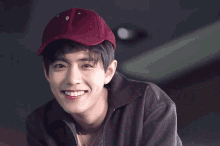 a young man wearing a burgundy baseball cap is smiling