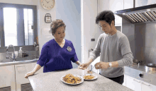 a man and a woman are preparing food in a kitchen with a clock on the wall that shows the time as 4:20