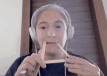 a woman wearing headphones holds a stick in her mouth