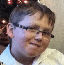 a young boy wearing glasses and a white shirt is making a funny face .