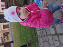 a little girl wearing a pink jacket and a white hat