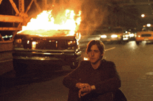 a man leans against a burning van on a street