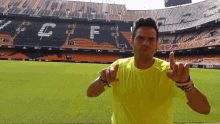 a man in a yellow shirt is pointing at the camera in front of a stadium that has the word coca cola on it