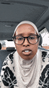 a woman wearing glasses and a scarf looks at the camera