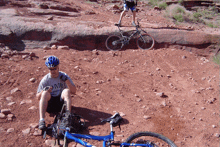 a man wearing a shirt that says mr sits on the ground next to a bike