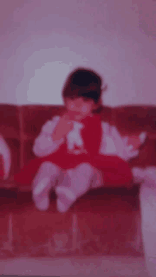 a little girl is sitting on a couch wearing a red dress