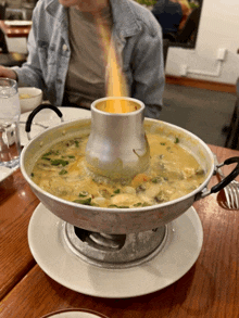 a person is sitting at a table with a pot of soup with flames coming out of it