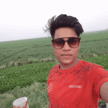 a young man wearing sunglasses and a red shirt that says sunny on it takes a selfie in front of a green field