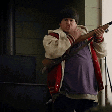 a man in a red and white jacket is holding a shotgun