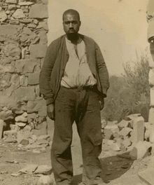 a man standing in front of a stone wall wearing a brown jacket