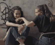 two women are sitting next to each other on the floor in front of a wall .