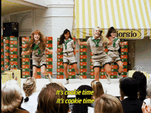 a group of girl scouts are performing in front of a crowd with the words it 's cookie time it 's cookie time above them