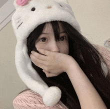 a girl wearing a white hello kitty hat is covering her face with her hand .