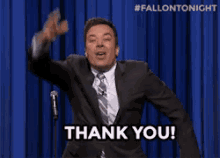 a man in a suit and tie says thank you in front of a blue curtain