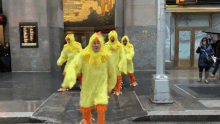 a group of people in yellow chicken costumes are walking down a street in front of a building that says comfort building