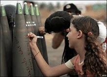 two girls are writing on a bunch of bullets with a marker