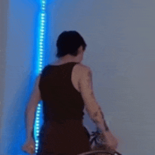 a man in a black tank top is standing in front of a wall with blue lights .