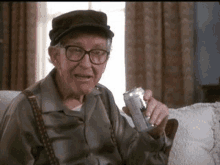 an old man is sitting on a couch holding a can of soda .