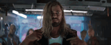 a man with long blonde hair and a beard is pointing to his chest