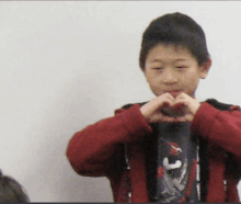 a young boy in a red jacket making a heart with his hands