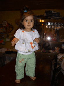 a little girl wearing a white shirt and green pants stands in front of a display case