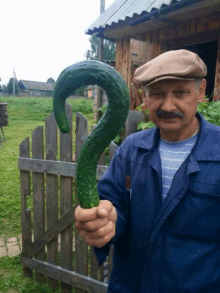 a man with a mustache holds a large green cucumber in the shape of a question mark