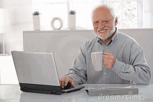 an older man is sitting at a desk using a laptop computer while holding a cup of coffee .