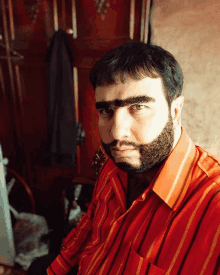 a man with a beard and big eyebrows wears a red striped shirt