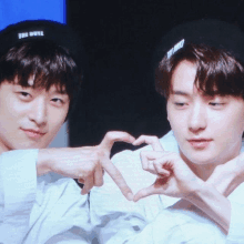 two young men are making a heart shape with their hands and one has a hat that says the boys