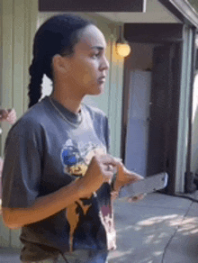 a woman in a t-shirt is standing in front of a building holding a cell phone .