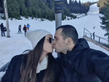 a man and a woman are kissing in front of a ski slope