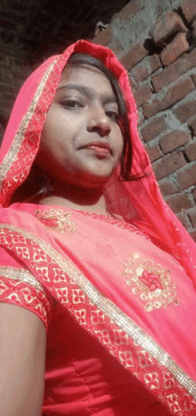 a woman in a pink dress and red veil is taking a picture of herself in front of a brick wall .