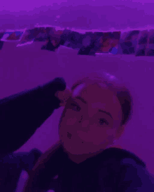 a girl is taking a selfie in front of a purple wall with pictures hanging on it .