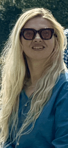 a woman wearing sunglasses and a blue shirt is smiling