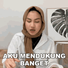 a woman wearing a hijab says aku mendukung banget in front of a monstera leaf