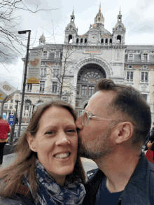 a man kisses a woman on the cheek in front of a building that has a sign that says ' antwerp '